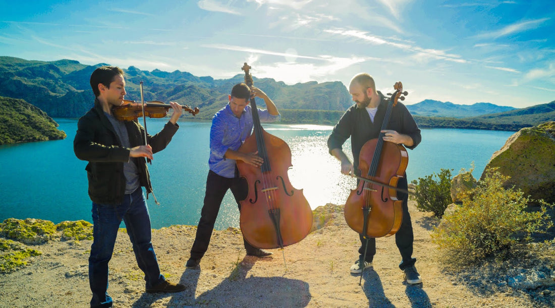 3 men playing instruments in front of a beautiful body of water