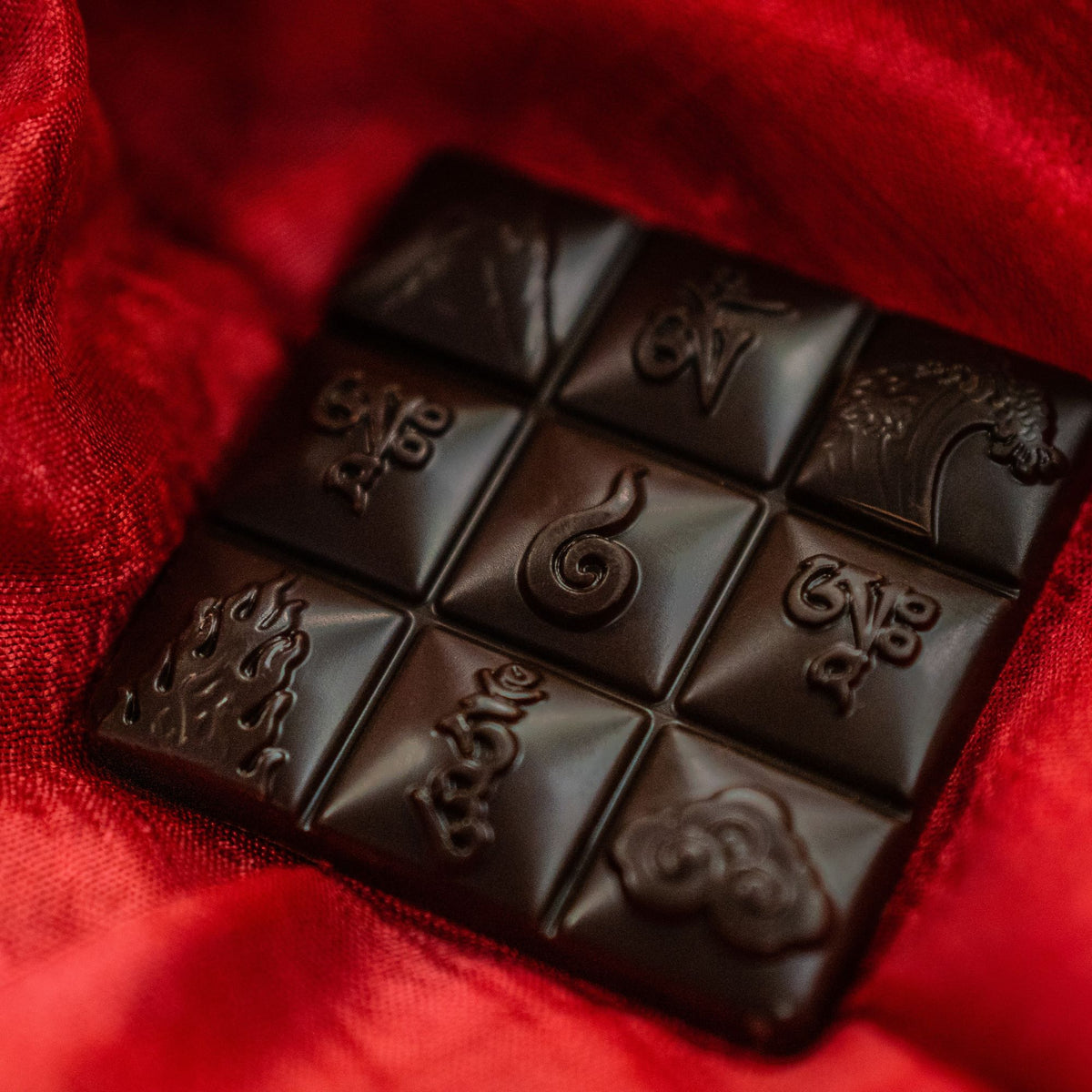 Dark chocolate Wei of Chocolate bar embossed with symbols, resting on red silk fabric